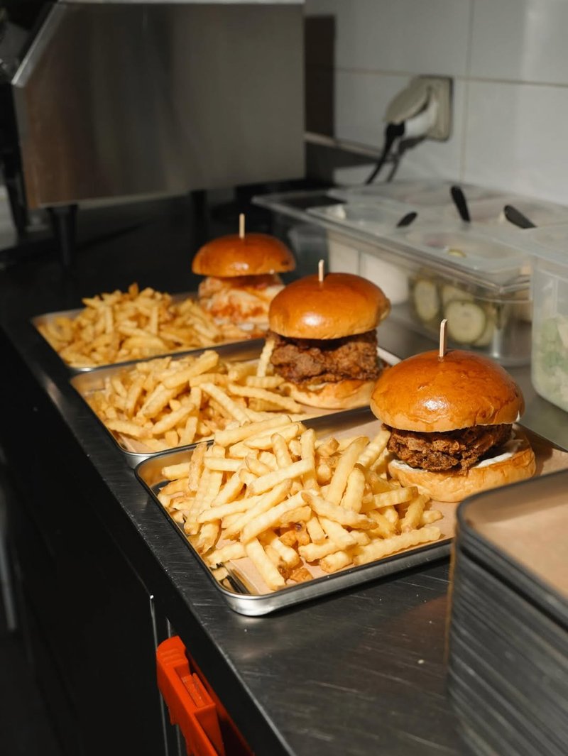 Three KANA fried chicken burgers with fries on the pass