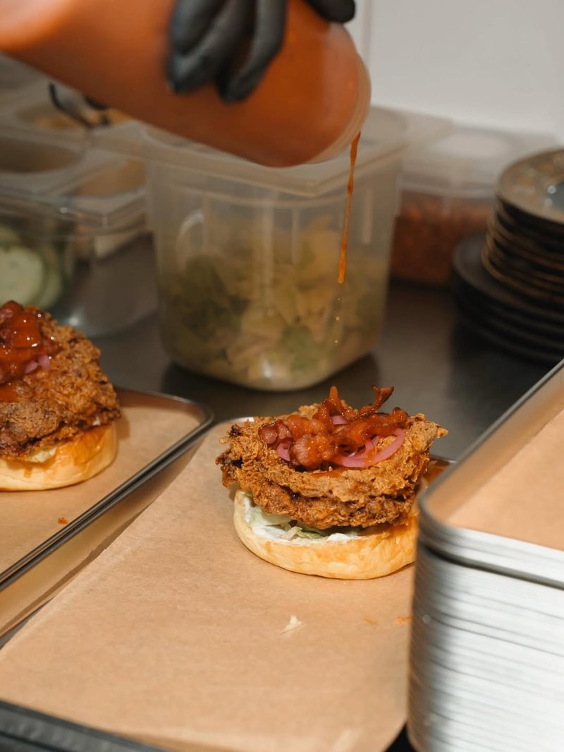 Sauce being drizzled on a KANA burger